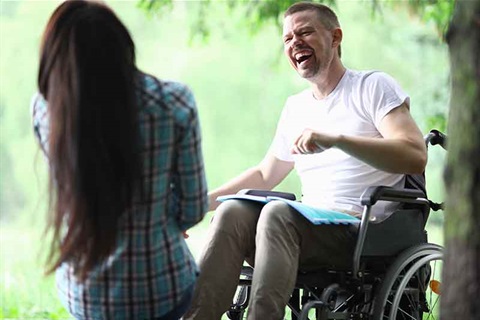 Young man in wheelchair with companion laughing