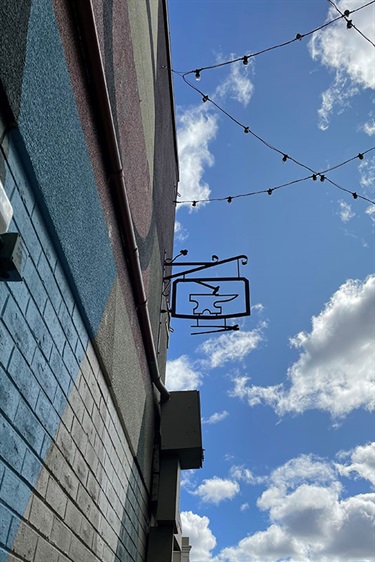 Metal anvil attached to roof along Blacksmiths Lane with festoon lights above