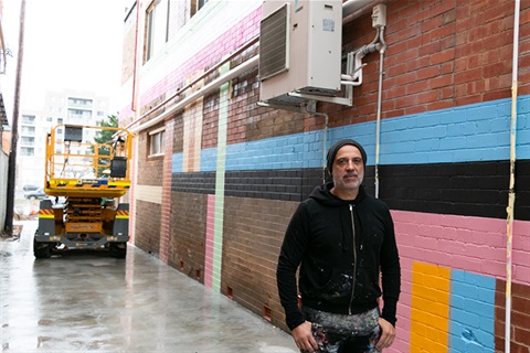 Photo of artist Yanni Pounartzis in No Name Lane with mural painting underway